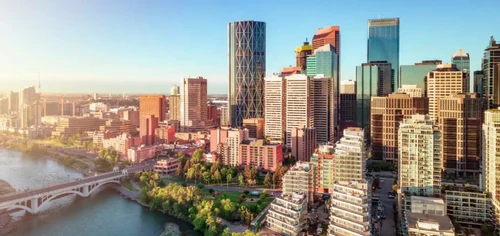 The Downtown Calgary skyline with Bow River and modern high-rise buildings under a clear blue sky at sunset.