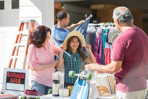 Family hosting a garage sale with a girl trying on a hat.